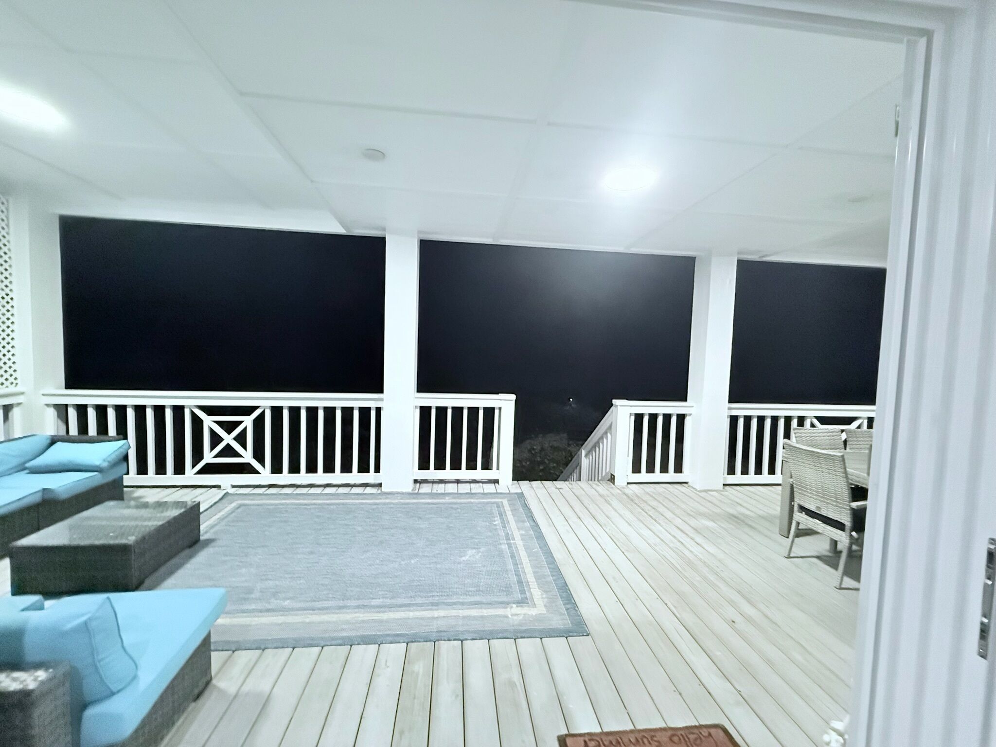 A covered outdoor area with a wooden deck, a seating area with cushions, and a view of the night sky.