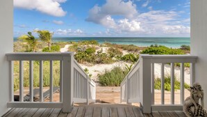 A wooden deck with white railings leading to a beach view.