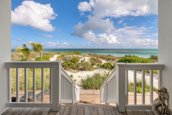 A wooden deck with white railings leading to a beach view.