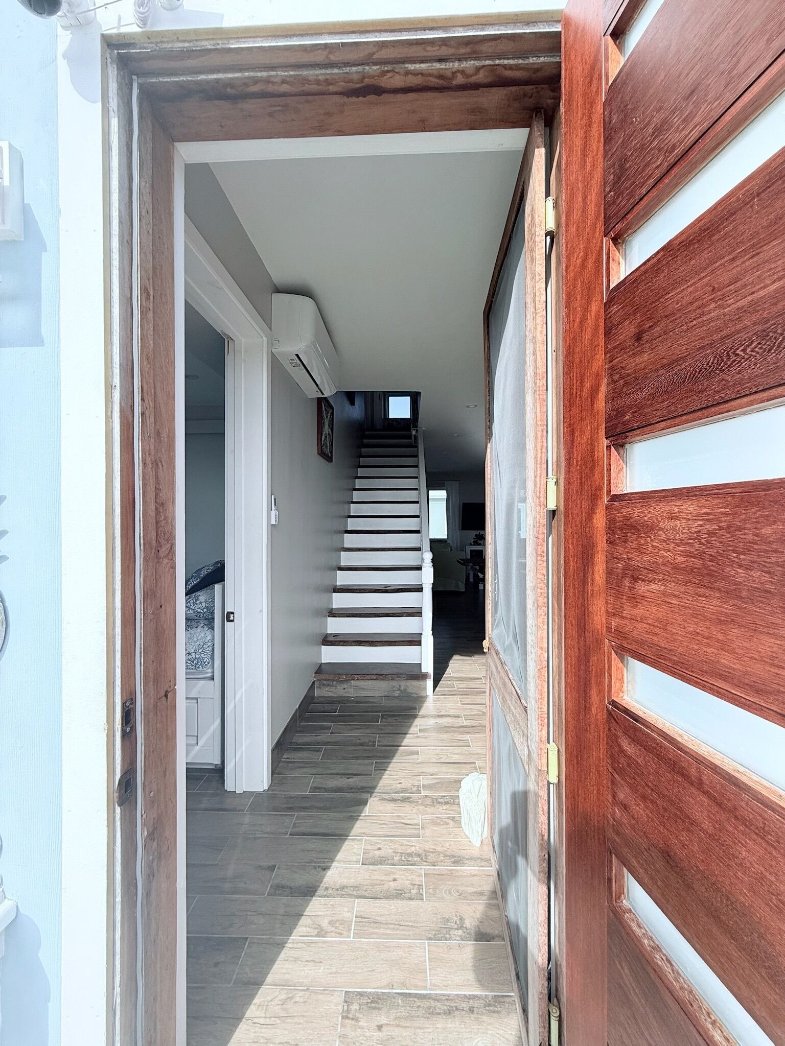 Un couloir avec une porte en bois, un escalier et un appareil de climatisation blanc.