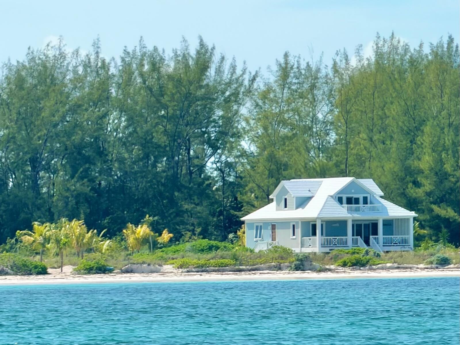 A coastal house with a balcony, surrounded by a beach and dense forest.