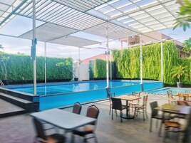 An outdoor pool area with a covered patio, seating, and a view of a building with a red roof.