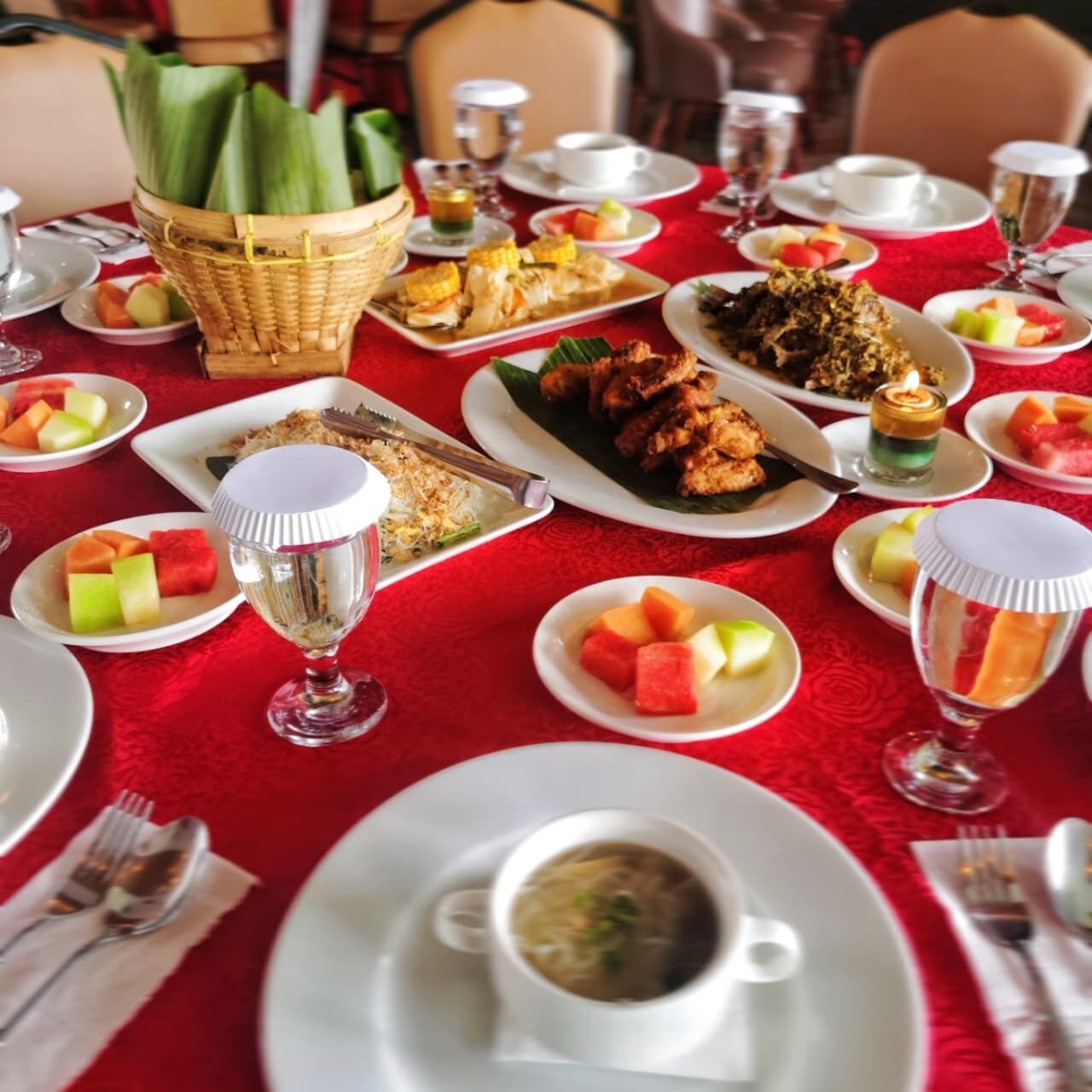 Une table dressée avec divers plats, notamment des fruits de mer, du riz et des fruits, sur une nappe rouge.