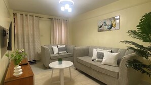 Ein Wohnzimmer mit einer Couch, einem Couchtisch, einem Fernseher und einer Pflanze.