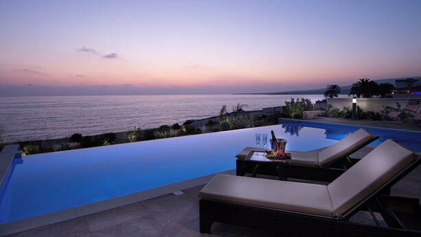 Un espace aménagé au bord de la piscine, avec des chaises longues et une table, d’où l’on peut admirer un plan d’eau au crépuscule.
