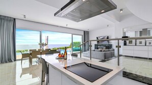Une cuisine moderne dotée d’un grand îlot central, d’un coin repas offrant une vue agréable et d’un espace de vie comprenant un canapé et un téléviseur.