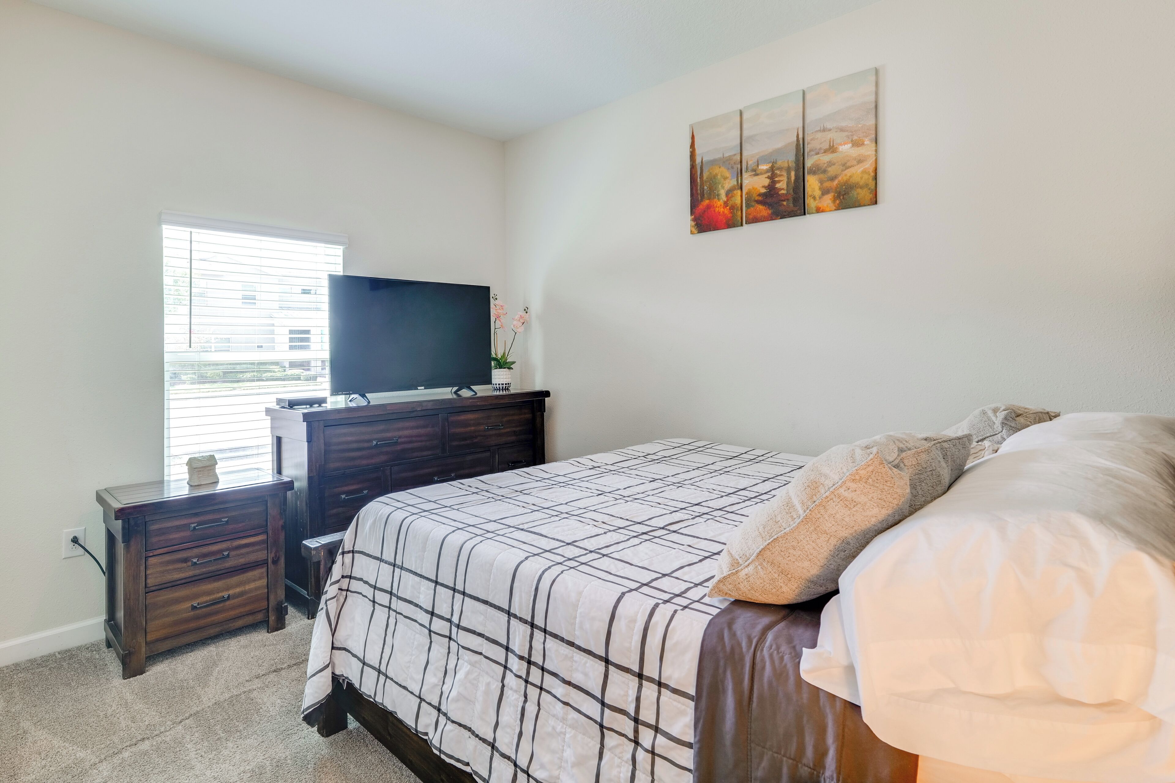 A bedroom with a bed, a dresser, a TV, and a window.