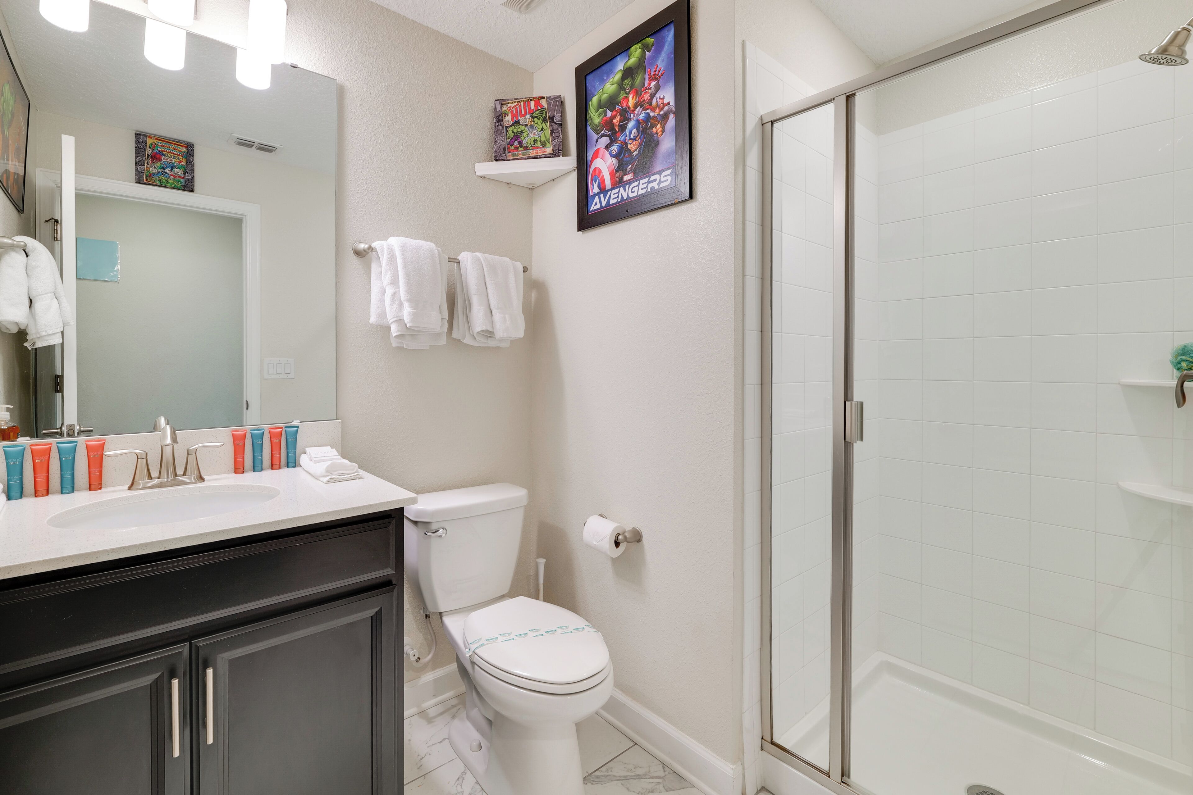 A bathroom with a toilet, sink, and shower. There are towels hanging on the wall and a framed poster above the toilet.