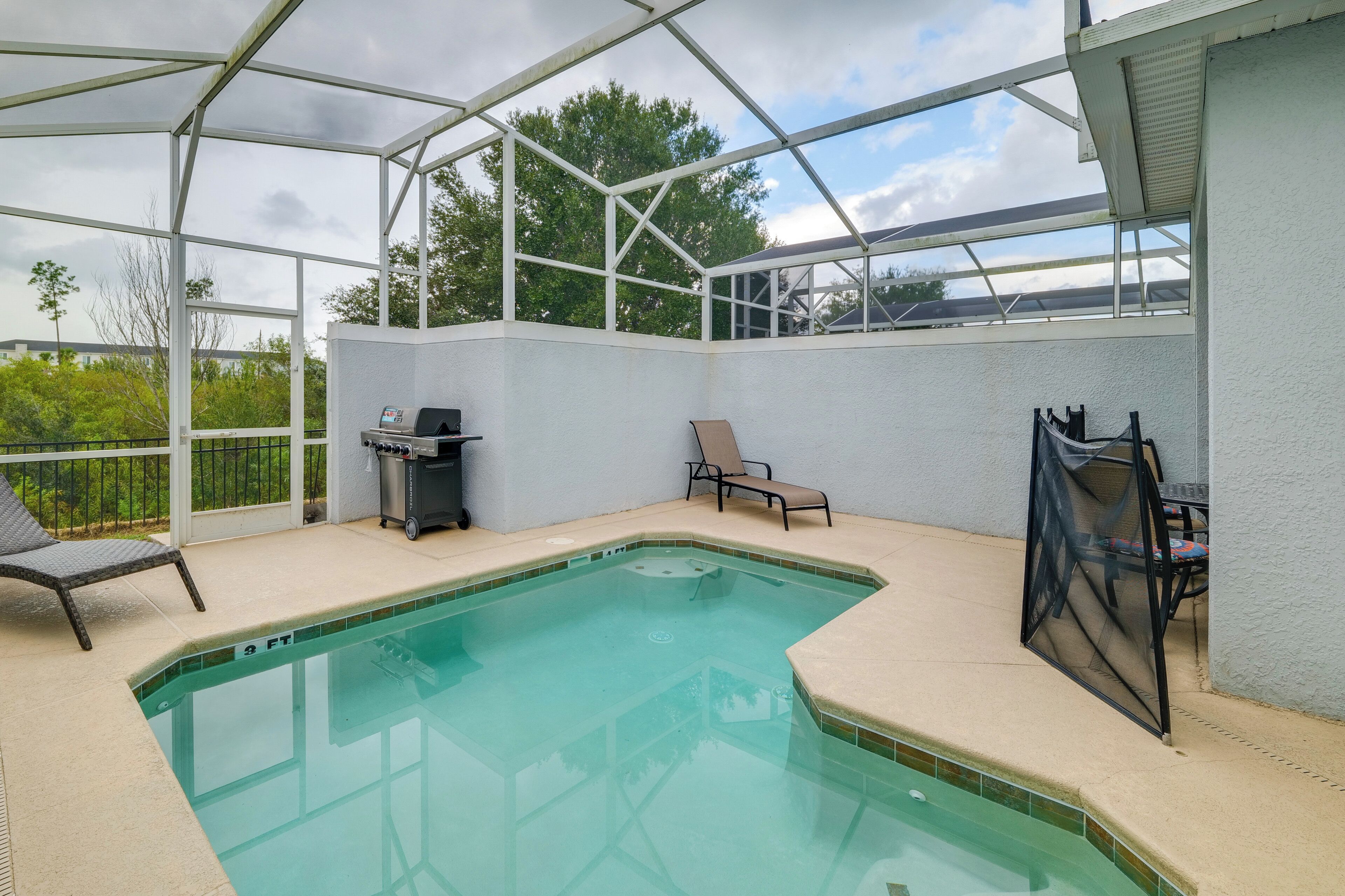 A covered outdoor swimming pool with a grill and lounge chairs.