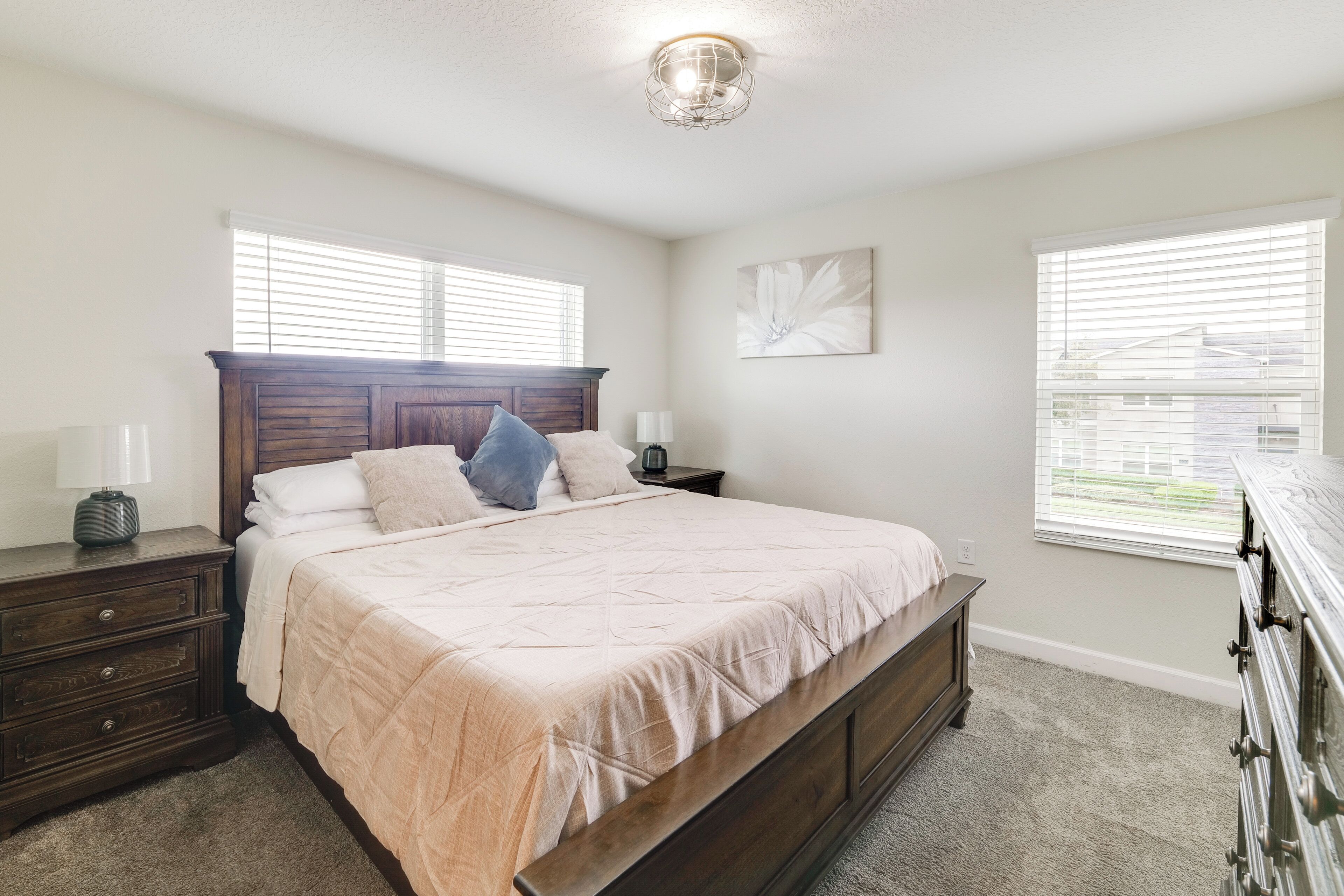 A bedroom with a large bed, two bedside tables, a dresser, and a ceiling light fixture.