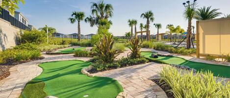 A miniature golf course with green artificial turf, palm trees, and stone pathways.