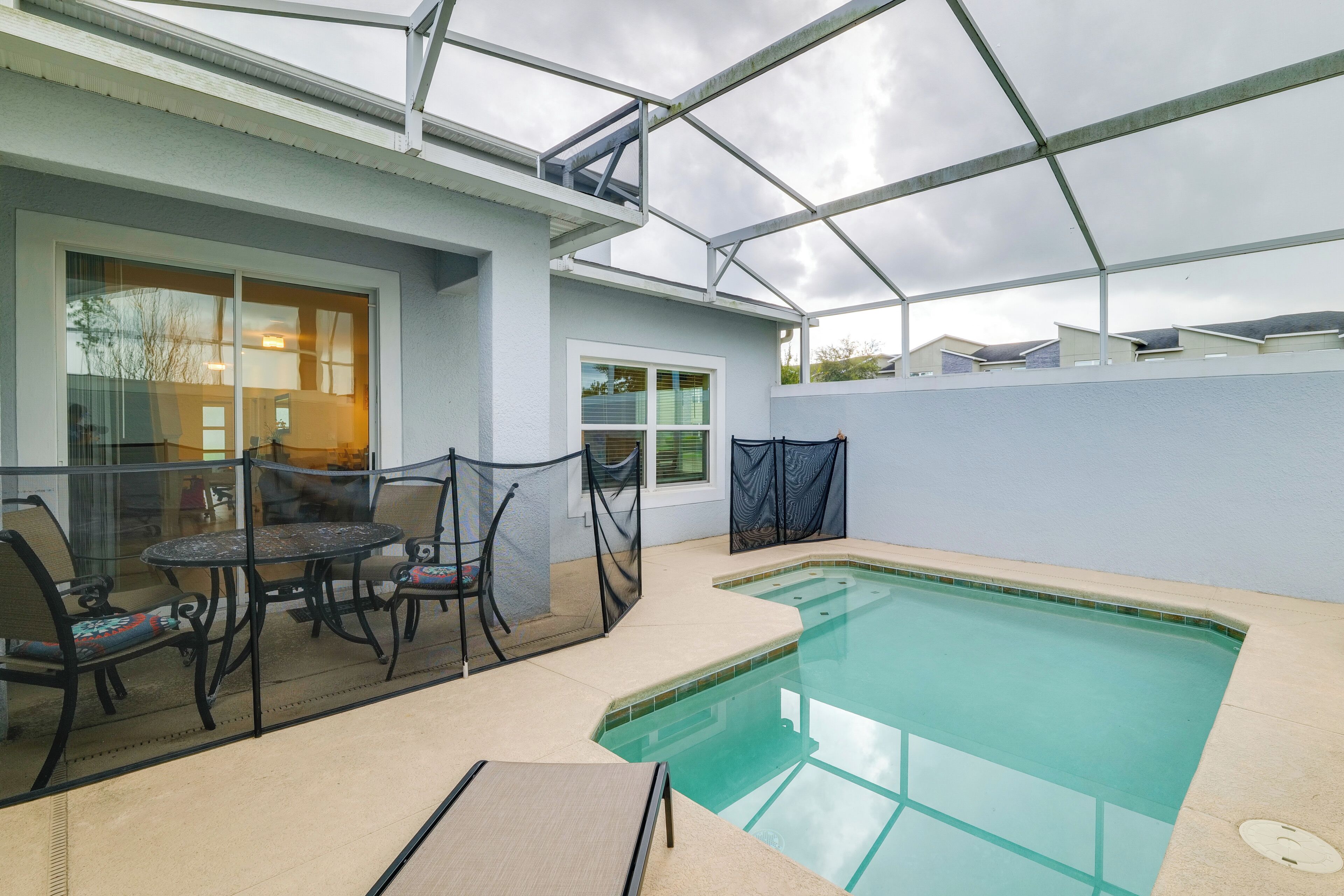 Une piscine extérieure couverte, dotée d’une structure en verre, un espace patio aménagé avec des sièges et une vue sur les maisons voisines.
