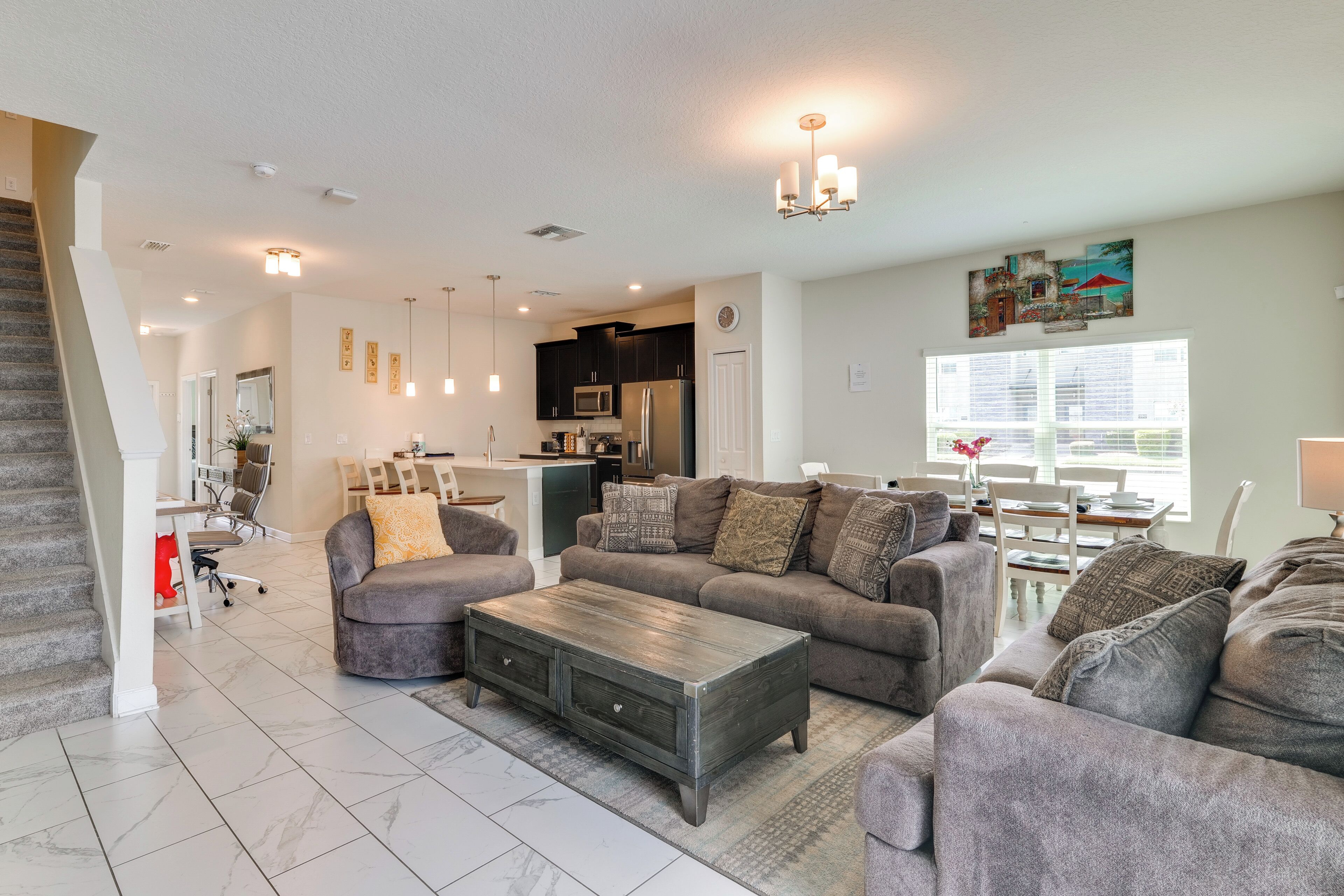 A spacious living room with a grey sofa set, a wooden coffee table, and a dining area with a white table and chairs.