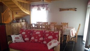 Une pièce chaleureuse avec un canapé en bois, une table à manger avec des chaises, un escalier et une fenêtre avec des rideaux.