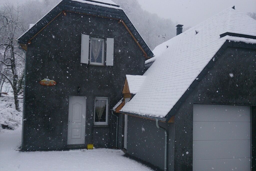 A dark-colored house with a white door, a garage, and a snow-covered roof.