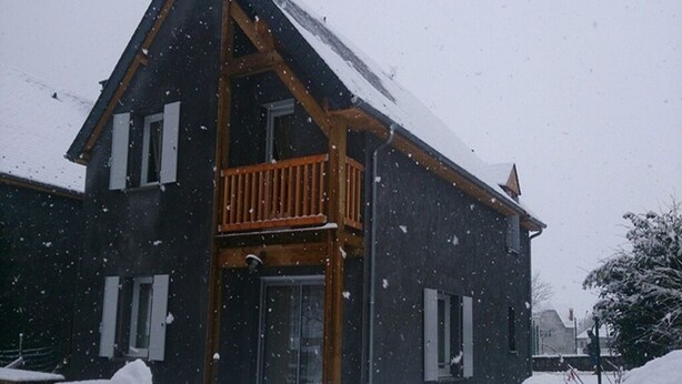 Une maison à deux étages avec un balcon en bois, entourée de neige.