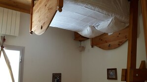 Une pièce avec un lit superposé, des poutres en bois, une porte blanche et deux tableaux encadrés au mur.