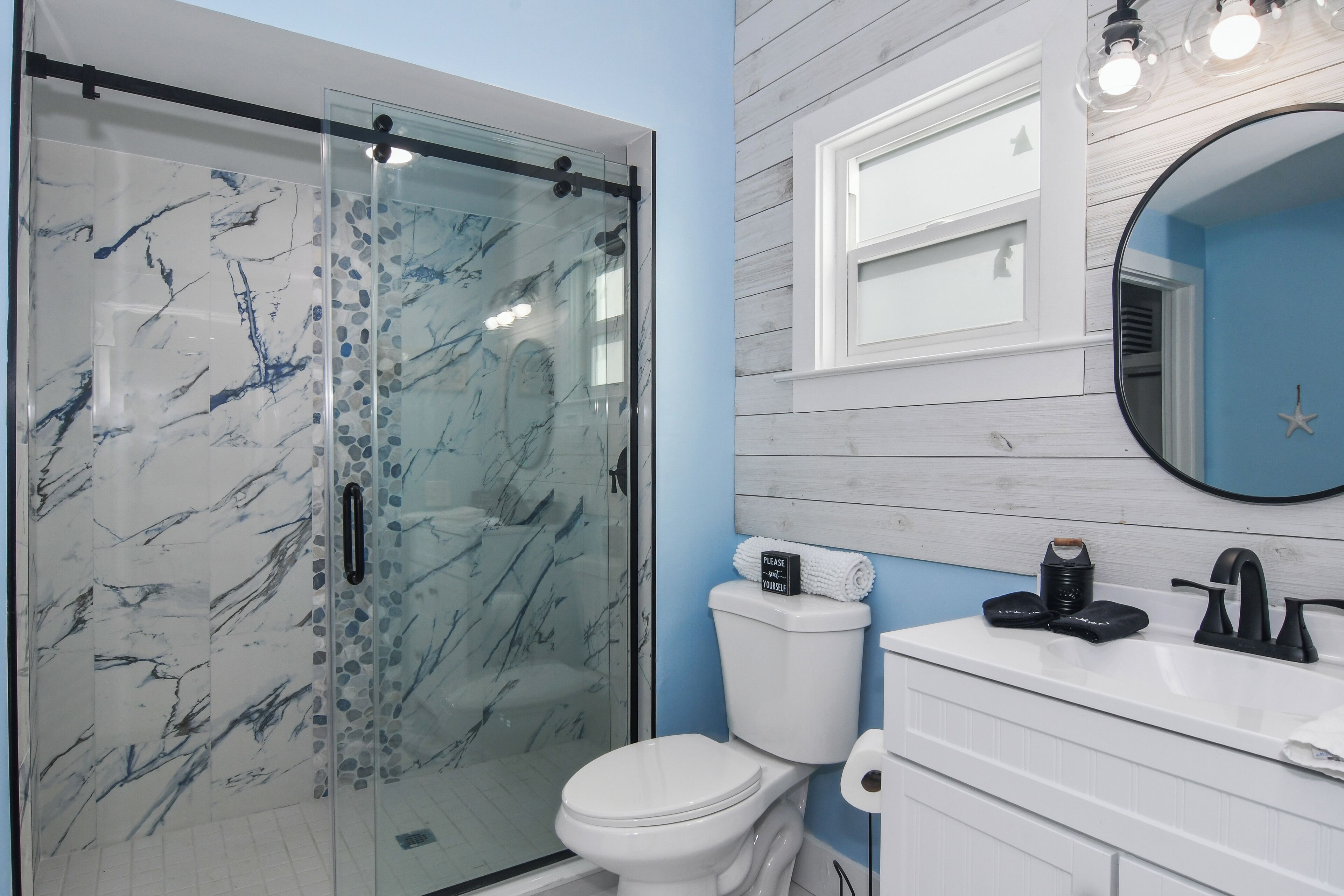 Un baño con ducha de vidrio, inodoro blanco y tocador con espejo.