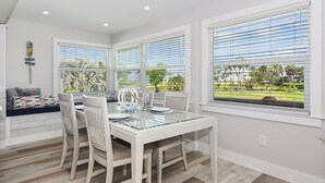 A dining area with a glass-top table, white chairs, and a view of the outdoors through large windows with blinds. - 1 Mi to Fort Myers Beach Access! Chic Coastal Home (Fort Myers Beach)