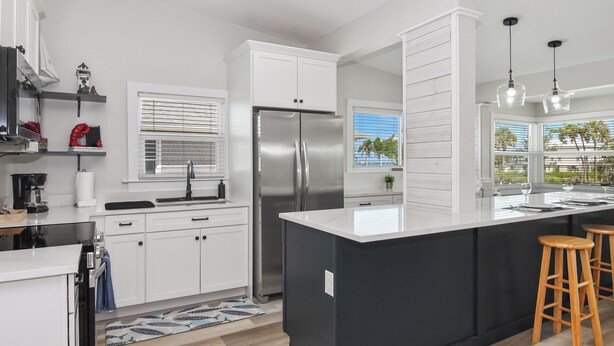 A modern kitchen with white cabinetry, a black island, wooden stools, and a stainless steel refrigerator. - 1 Mi to Fort Myers Beach Access! Chic Coastal Home (Fort Myers Beach)