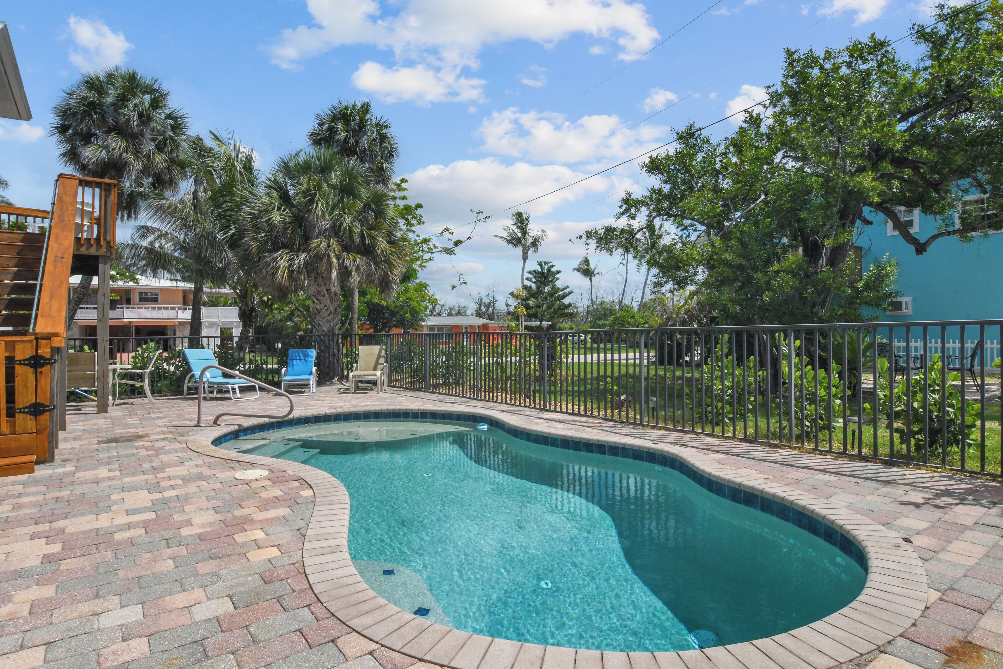 A swimming pool with a brick deck, lounge chairs, and palm trees.