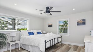 A bedroom with a bed, a ceiling fan, a nightstand, a lamp, and a window with blinds. - 1 Mi to Fort Myers Beach Access! Chic Coastal Home (Fort Myers Beach)