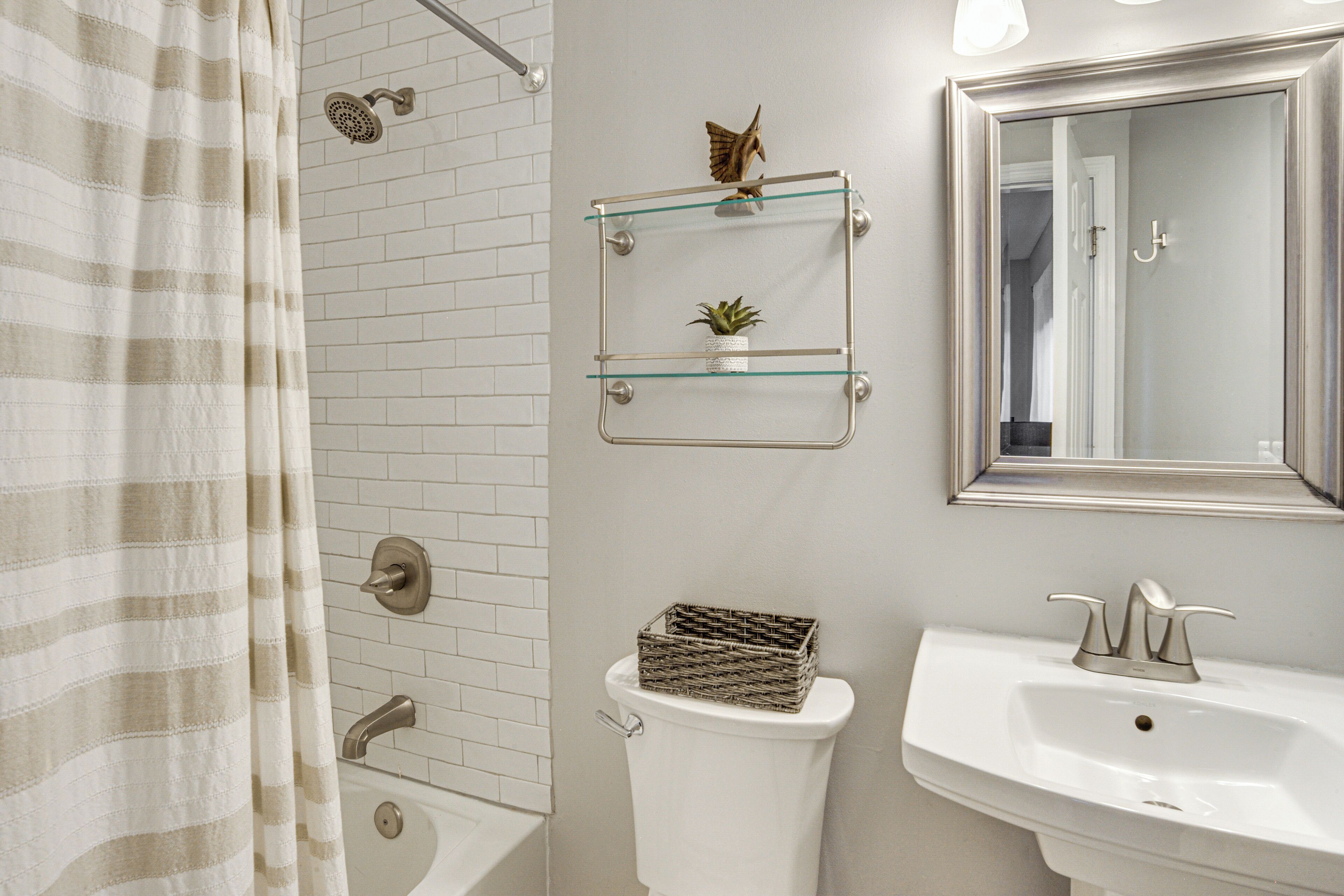 A bathroom with a shower, toilet, and sink. There are glass shelves above the toilet and a mirror above the sink.