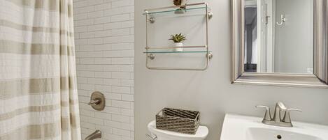 A bathroom with a shower, toilet, and sink. There are glass shelves above the toilet and a mirror above the sink.
