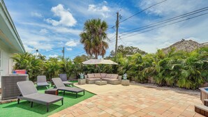 Eine Außenpatio mit Sitzgelegenheit, darunter eine Couch und Lounge-Stühle, umgeben von üppiger Bepflanzung und einer Palme.