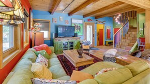 Ein gemütliches Wohnzimmer mit Holzbalkendecke, einem grünen Sofa, einem Holztisch und einem Fernseher auf einer Kommode.