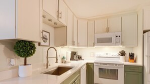 Una cocina con gabinetes blancos, microondas, estufa y pileta.