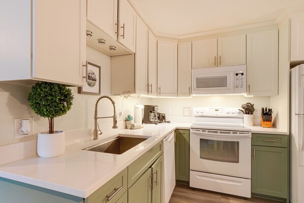Una cocina con gabinetes blancos, microondas, estufa y pileta.