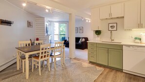 Una cocina moderna con armarios blancos, un comedor con mesa y sillas de madera, y vistas a una sala de estar.