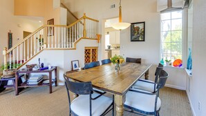 A spacious dining area with a wooden table and chairs, a staircase, and a large window with natural light. - 1 Block to Bay: Pet-friendly Retreat in Alameda! (Alameda)