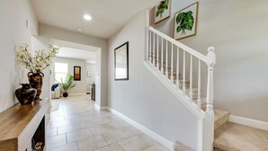 A hallway with a wooden console table, a vase with flowers, and a staircase with a white railing. - Group Getaway 5 Mi to Dtwn Visalia (Visalia)