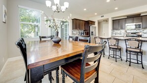 A spacious kitchen with dark wooden cabinets, a large island with bar stools, and a chandelier. - Group Getaway 5 Mi to Dtwn Visalia (Visalia)