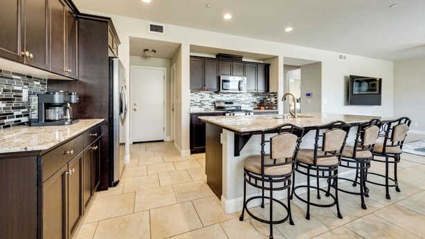 A modern kitchen with dark cabinetry, a central island with bar stools, and a tiled backsplash. - Group Getaway 5 Mi to Dtwn Visalia (Visalia)
