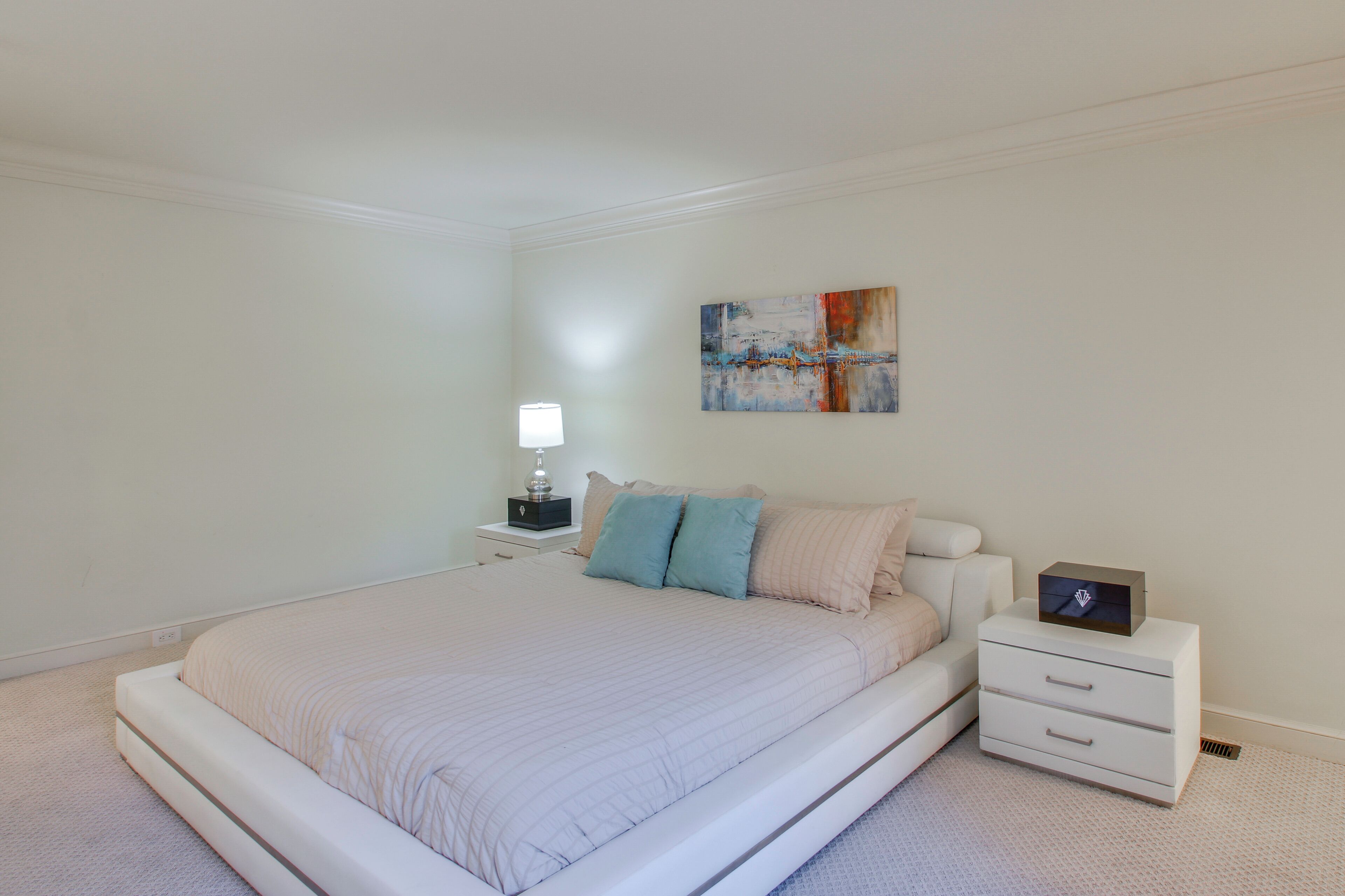 A bedroom with a bed, nightstand, lamp, and abstract painting.
