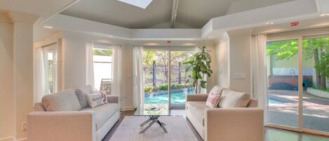 A modern hotel lobby with two sofas, a coffee table, and a large sliding glass door leading to a pool area.