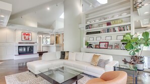 A spacious living room with a sectional sofa, a glass coffee table, and a bookshelf filled with books and decorative items. - 1 Mi to OU! Group Getaway w/ Game Room, Pool (Norman)