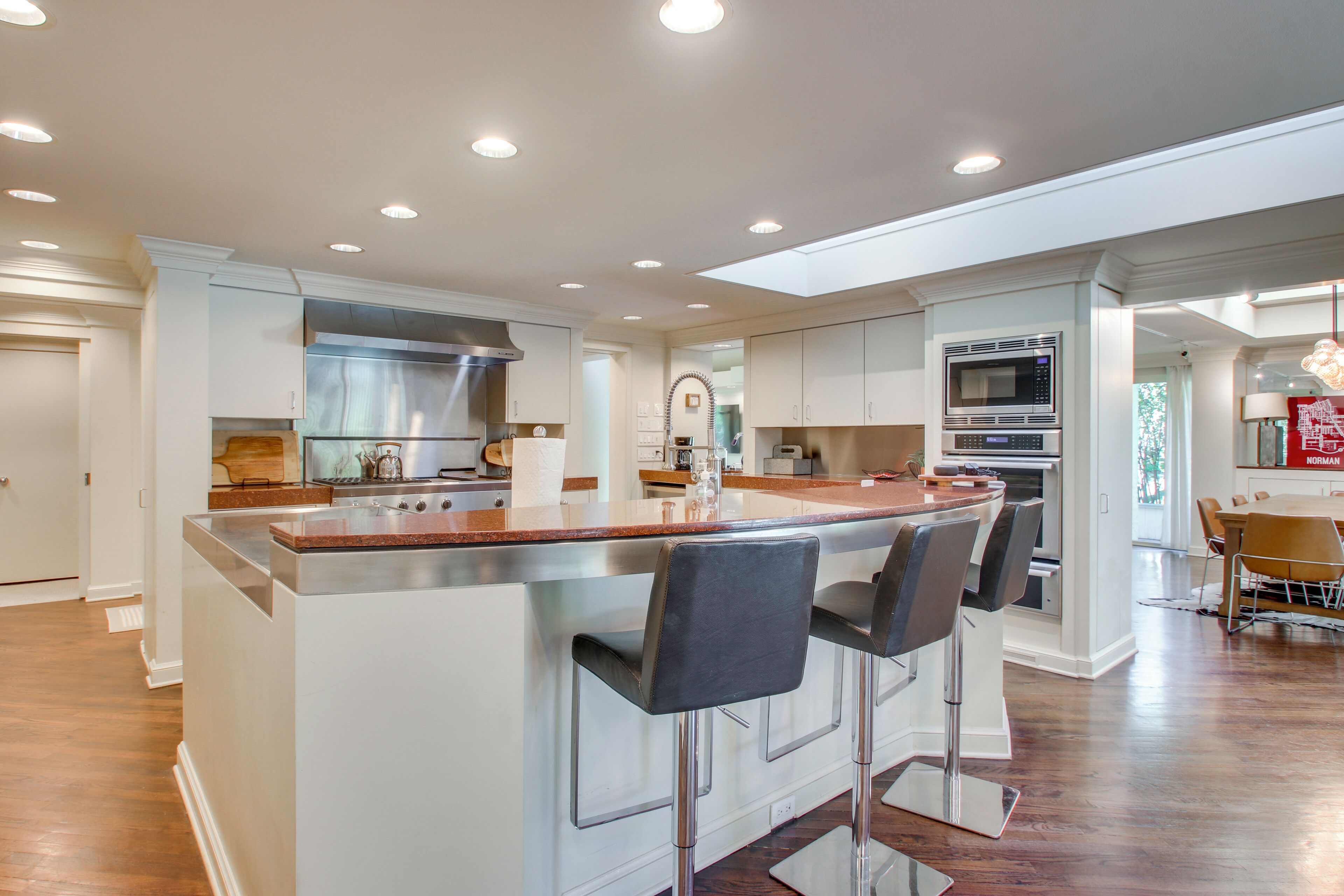 A modern kitchen with a central island, bar stools, stainless steel appliances, and a dining area with a table and chairs.