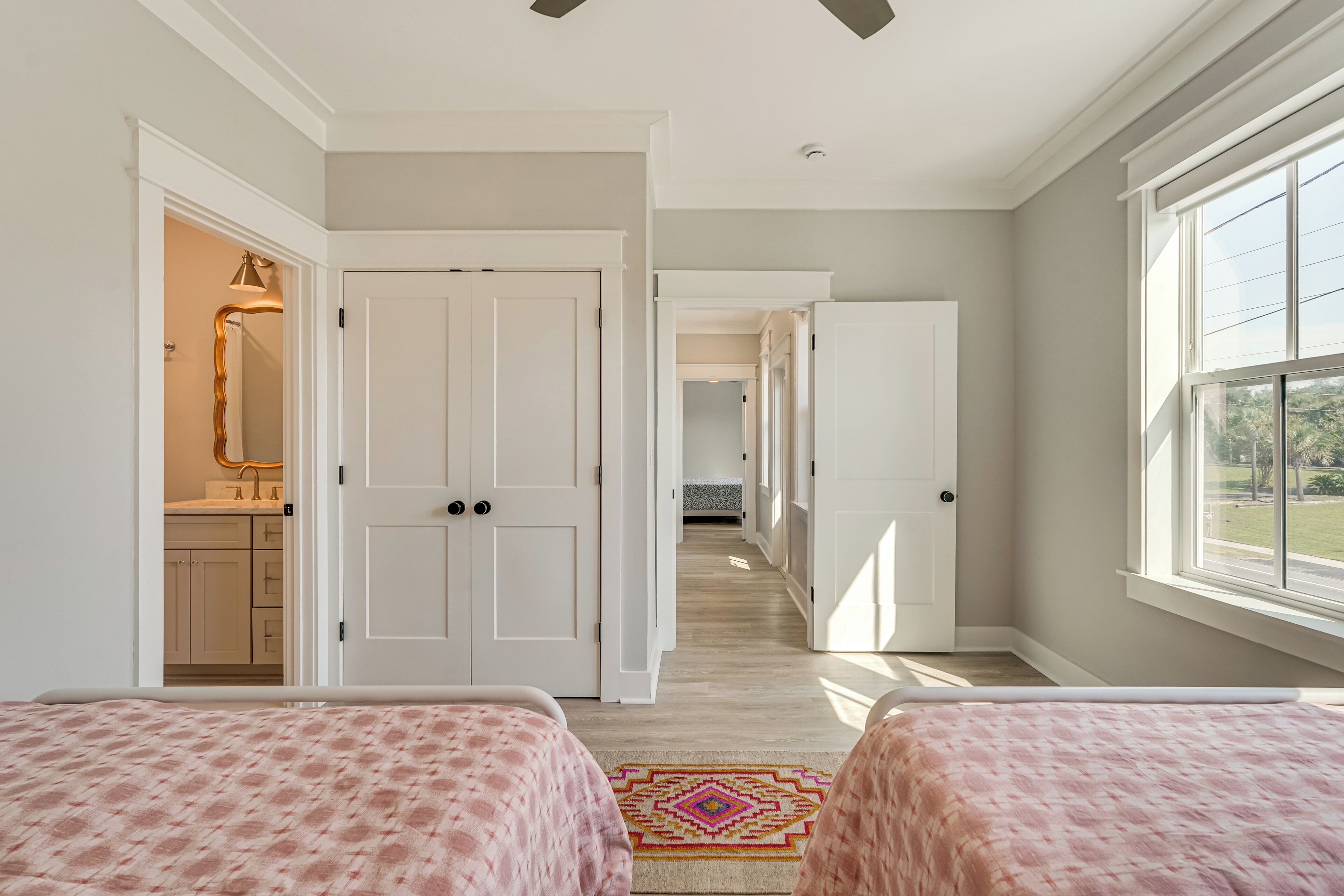 A bedroom with two beds, a bathroom with a mirror, and a view of a garden through a window.