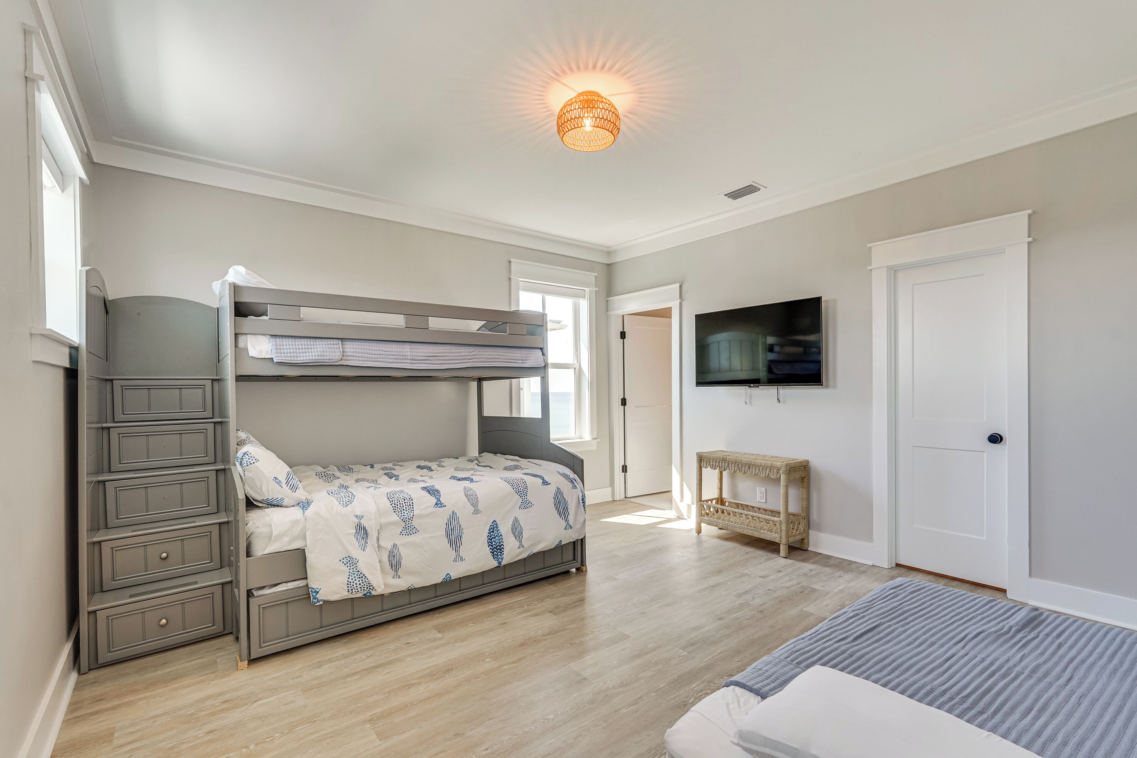 Une chambre avec un lit superposé, une commode à tiroirs, un téléviseur fixé au mur et une porte.