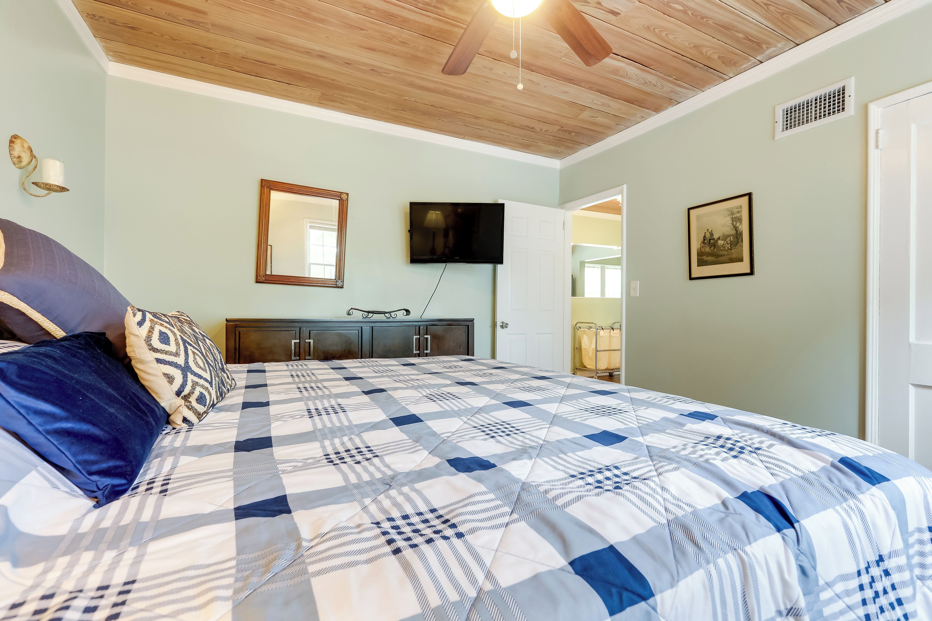 A bedroom with a large bed, a ceiling fan, a television, and a door leading to another room.