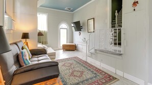 A living room with a leather sofa, a patterned rug, a staircase, and a white door. - Historic Sunrise House w/ Game Room: Near Beach! (Fort Pierce)