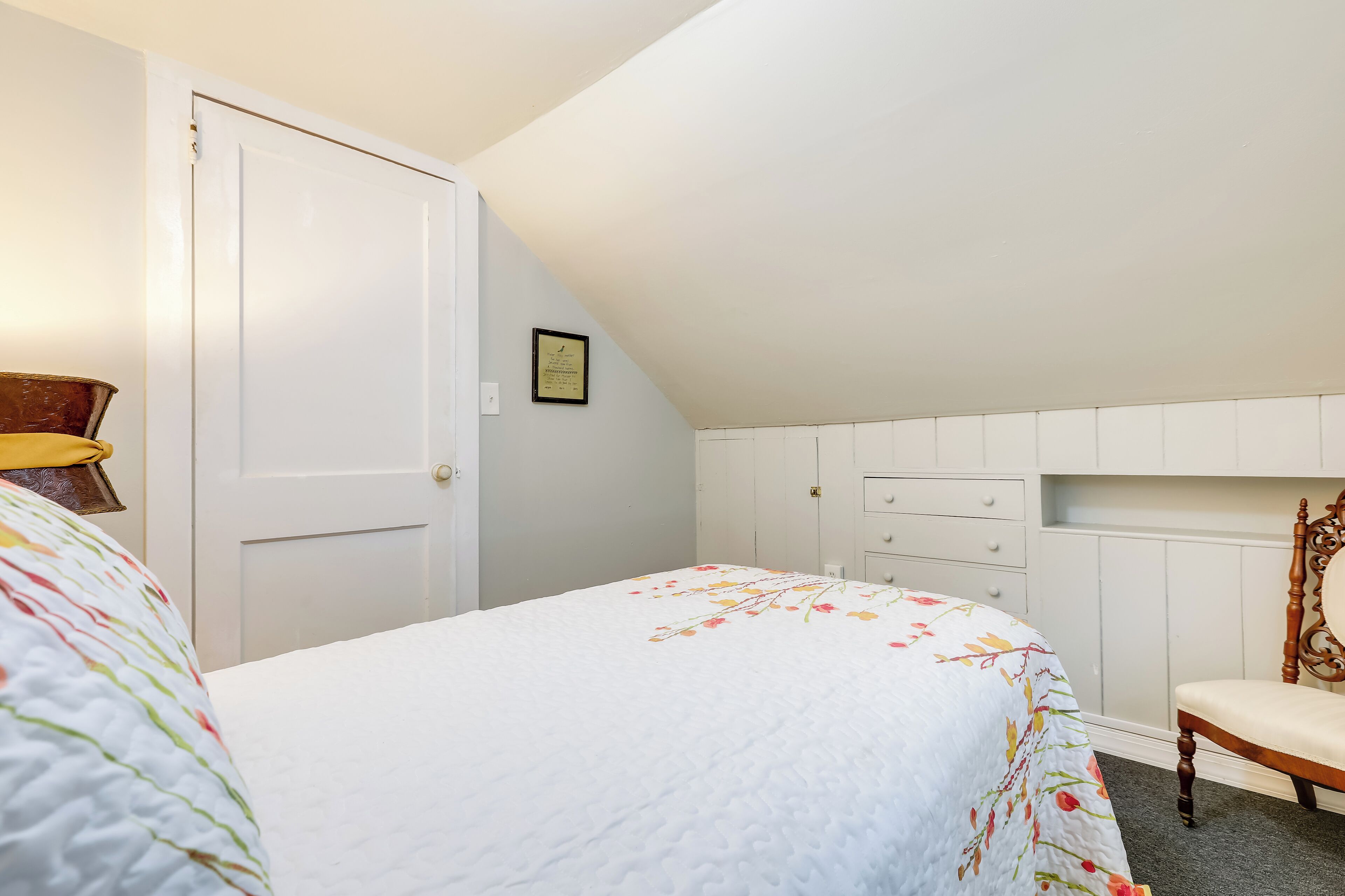 A bedroom with a bed, a chair, a door, and a wall-mounted shelf.