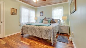 A bedroom with a wooden ceiling, a bed with a patterned bedspread, two bedside tables with lamps, and a framed picture on the wall. - Historic Sunrise House w/ Game Room: Near Beach! (Fort Pierce)