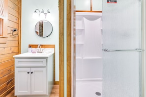 Un baño con tocador de madera, espejo redondo y cabina de ducha.