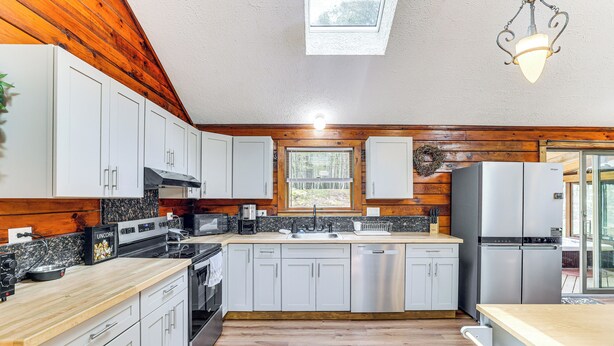 A modern kitchen with wooden paneling, stainless steel appliances, and a skylight. - Hot Tub & Covered Deck! Long Pond Log Cabin (Long Pond)