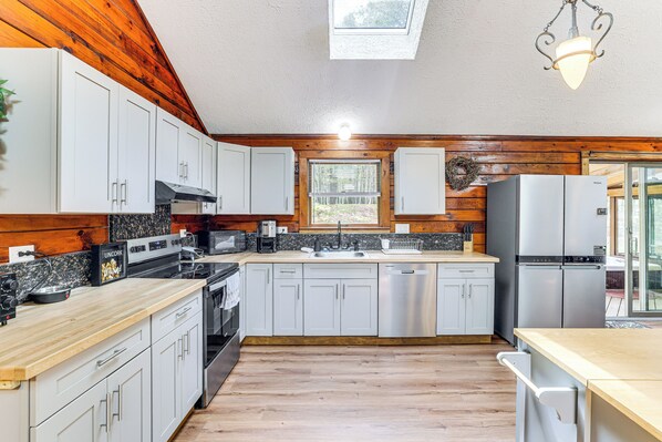 A kitchen with wooden walls, white cabinets, stainless steel appliances, and a skylight.
